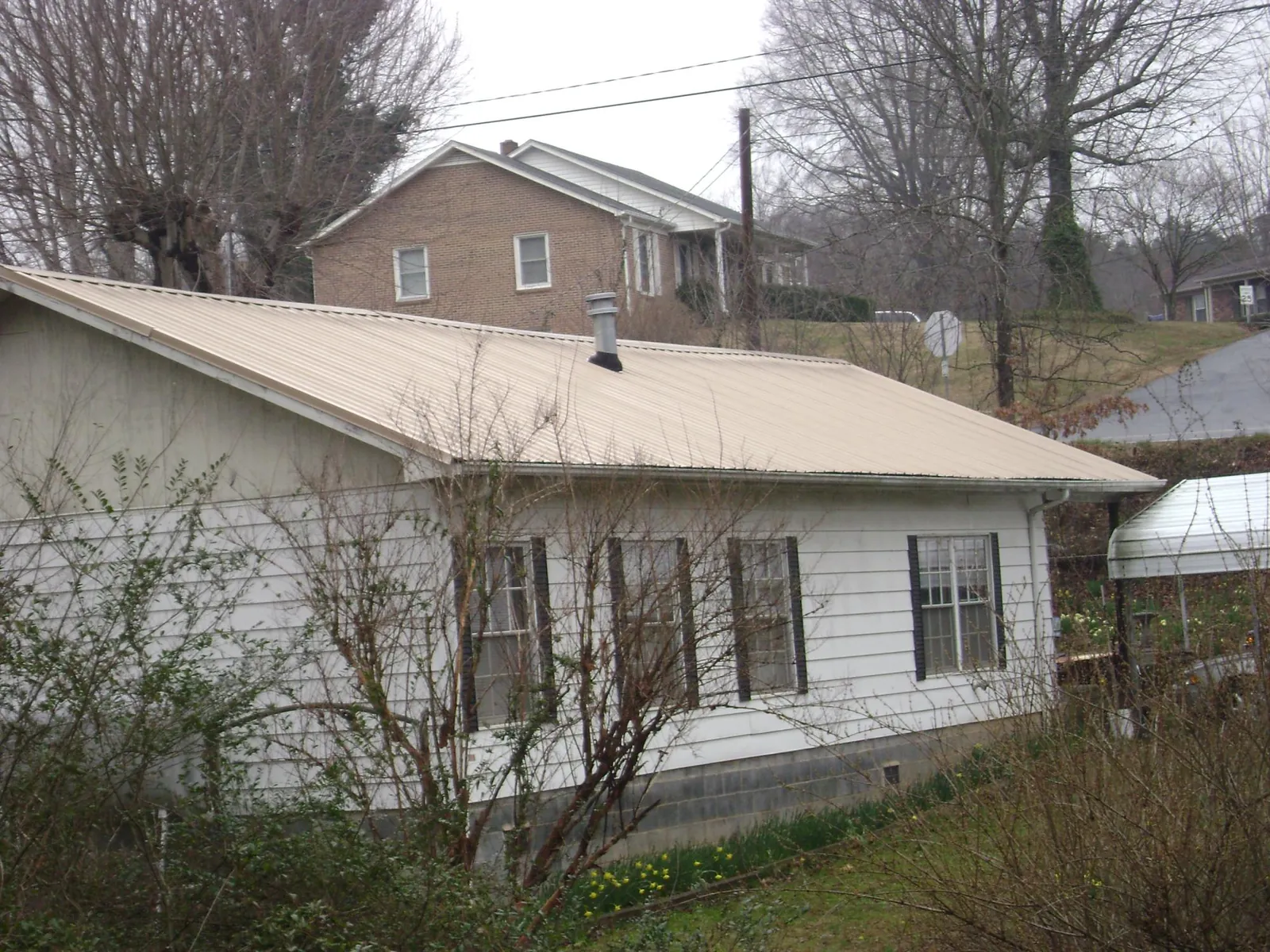 Tan metal roof on a white sided house set into a hillside — Commercial Roofing by Roofing Brothers in Milan